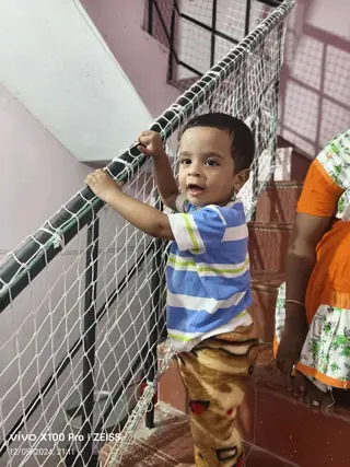 Toddler standing safely behind a green YPL balcony safety net in a Chennai apartment